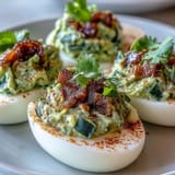 Guacamole-filled deviled eggs topped with diced tomato and jalapeño, a vibrant twist on a classic appetizer.
