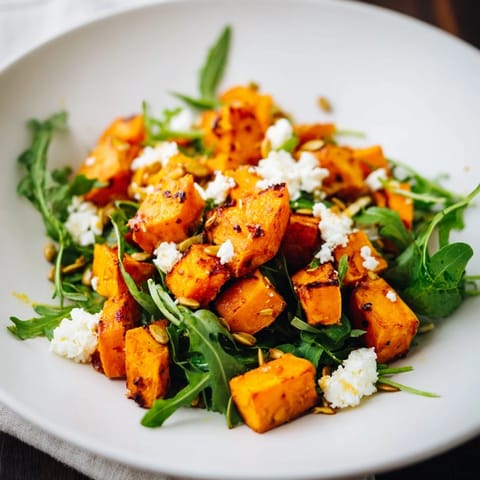 A vibrant roasted sweet potato salad featuring caramelized sweet potatoes, peppery arugula, and creamy feta on a rustic wooden table.
