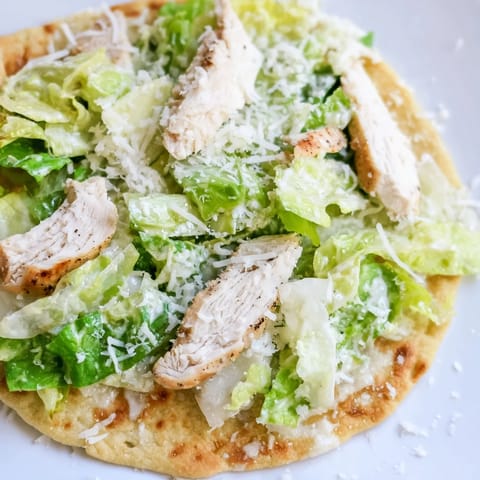 Sliced Chicken Caesar Flatbread on a white plate with fresh romaine, parmesan, and cherry tomatoes.  