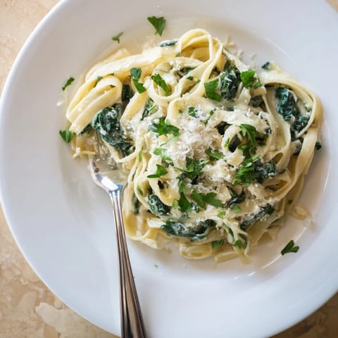 Creamy Garlic Spinach Pasta served in a white bowl, the fettuccine strands coated in a luscious pale green sauce with wilted spinach leaves.