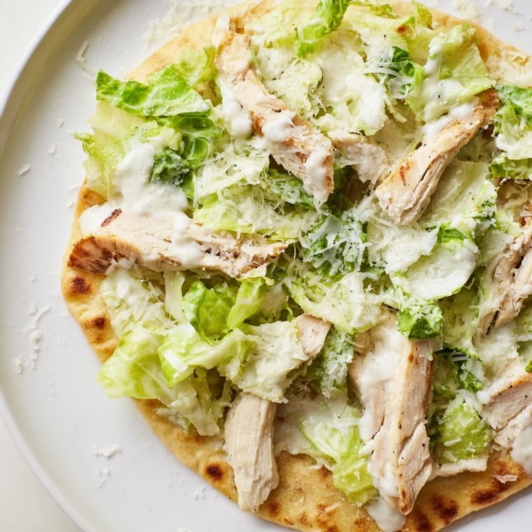 Warm, baked Chicken Caesar Flatbread topped with seasoned chicken, creamy Caesar, and fresh veggies.