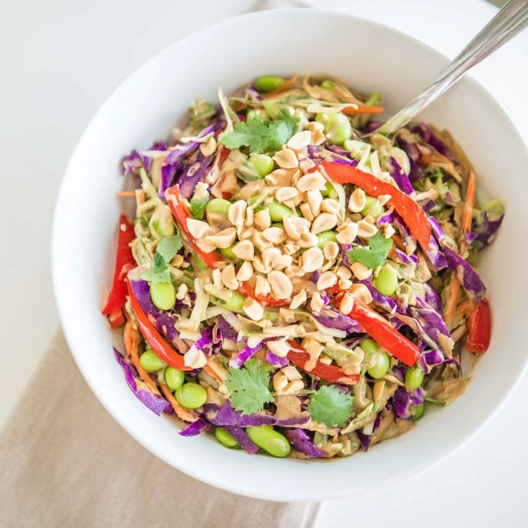 This vegetarian Thai-inspired Crunchy Thai Peanut Salad showcases vibrant vegetables and fresh cilantro, paired with lime wedges for a bright, tangy finish.
