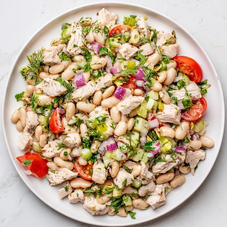 Freshly prepared Lemony White Bean Chicken Salad garnished with parsley and dill, tossed with red onion and cherry tomatoes for a bright, protein-packed lunch.