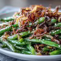 A vibrant bowl of sesame garlic green beans topped with golden crispy onions for a crunchy finish.